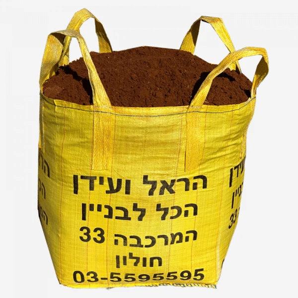 שק ענק של אדמת חמרה איכותית במשקל 450 ק"ג, בצבע אדום-חום טבעי, מתאים לגינה, דשא סינטטי ושתילה.
